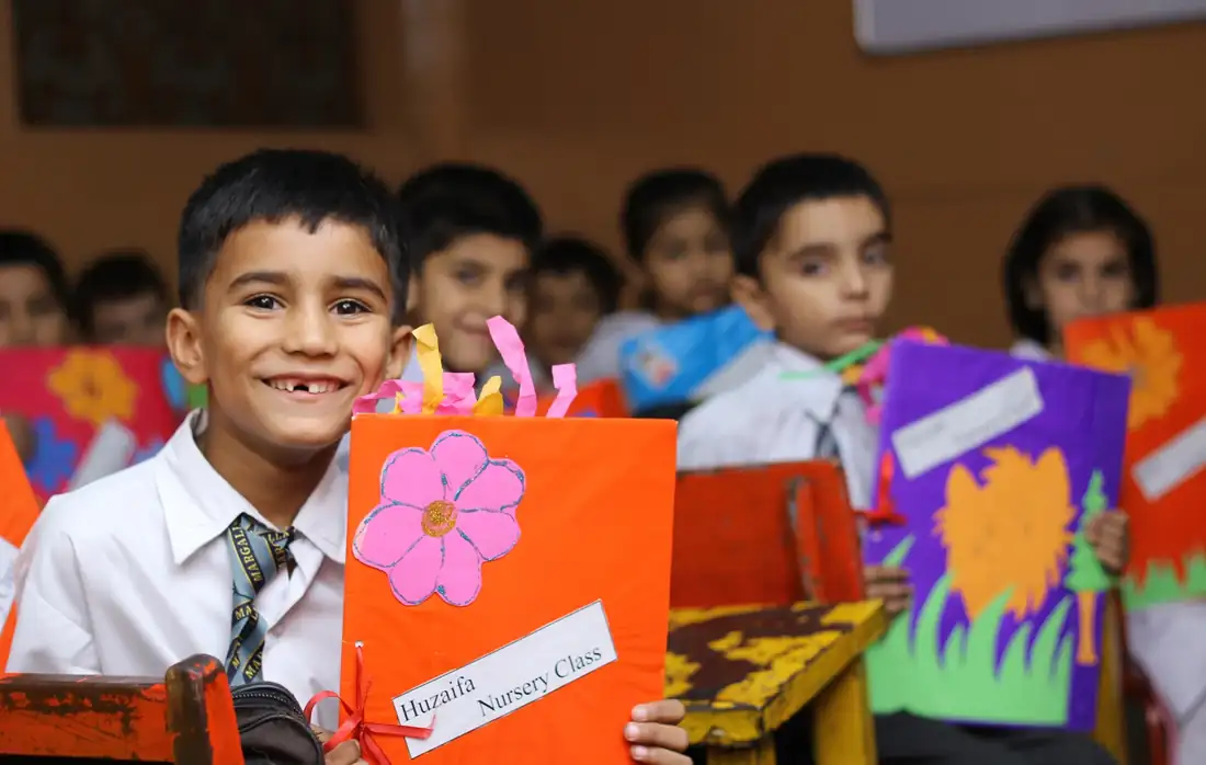 Smiling schoolboy holding up his nursery class project folder